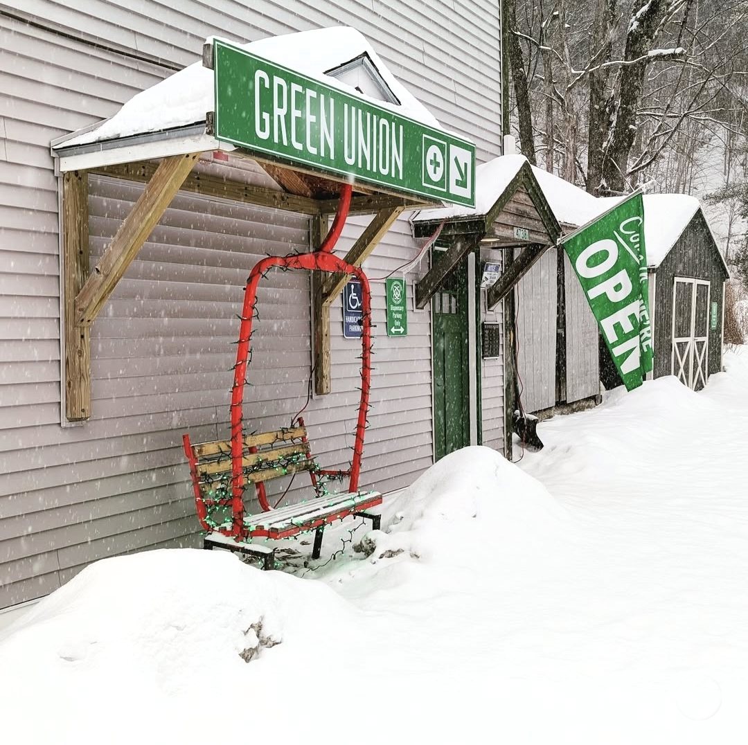 The front of Green Union Dispensary: a red chairlift bench under the green Green Union sign, with the store entrance beside it